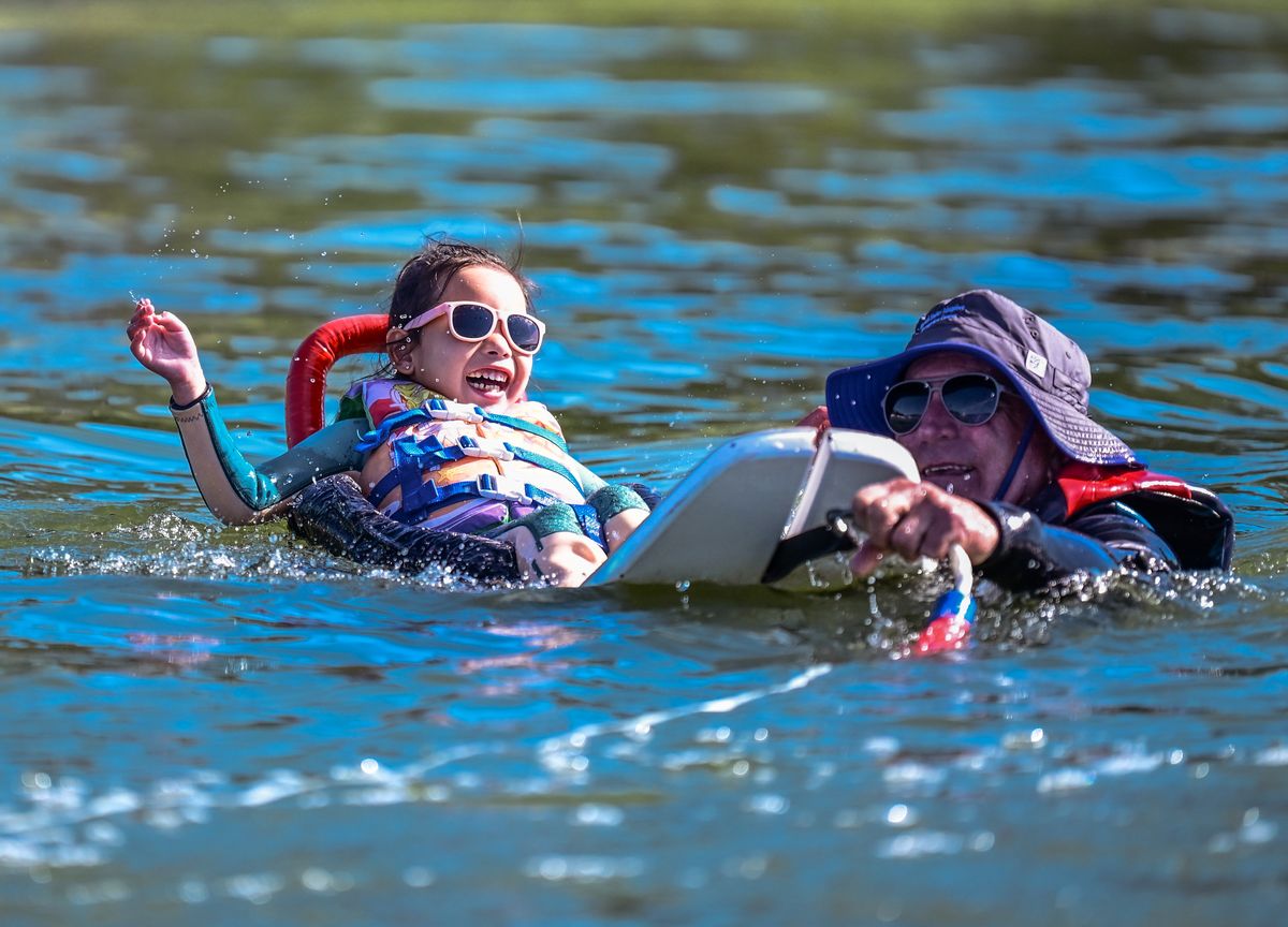 A girl in sunglasses laughs in Big Bear Lake beside her adaptive water ski while a USARC volunteer stays at her side.