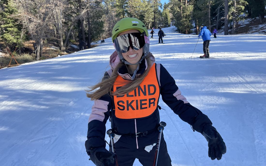 A smiling skier in an orange blind-skier bib heads down a groomed run at Big Bear.