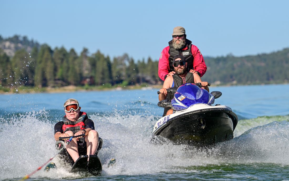 Two USARC volunteers on a personal watercraft run alongside a participant on a sit-ski across Big Bear Lake.